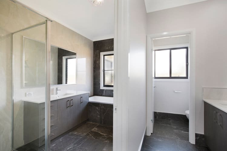 Grey and white bathroom with toilet, vanities, bath and shower