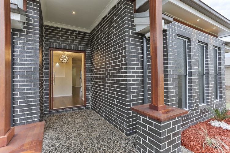 Entryway to dark brick home with wooden pillars