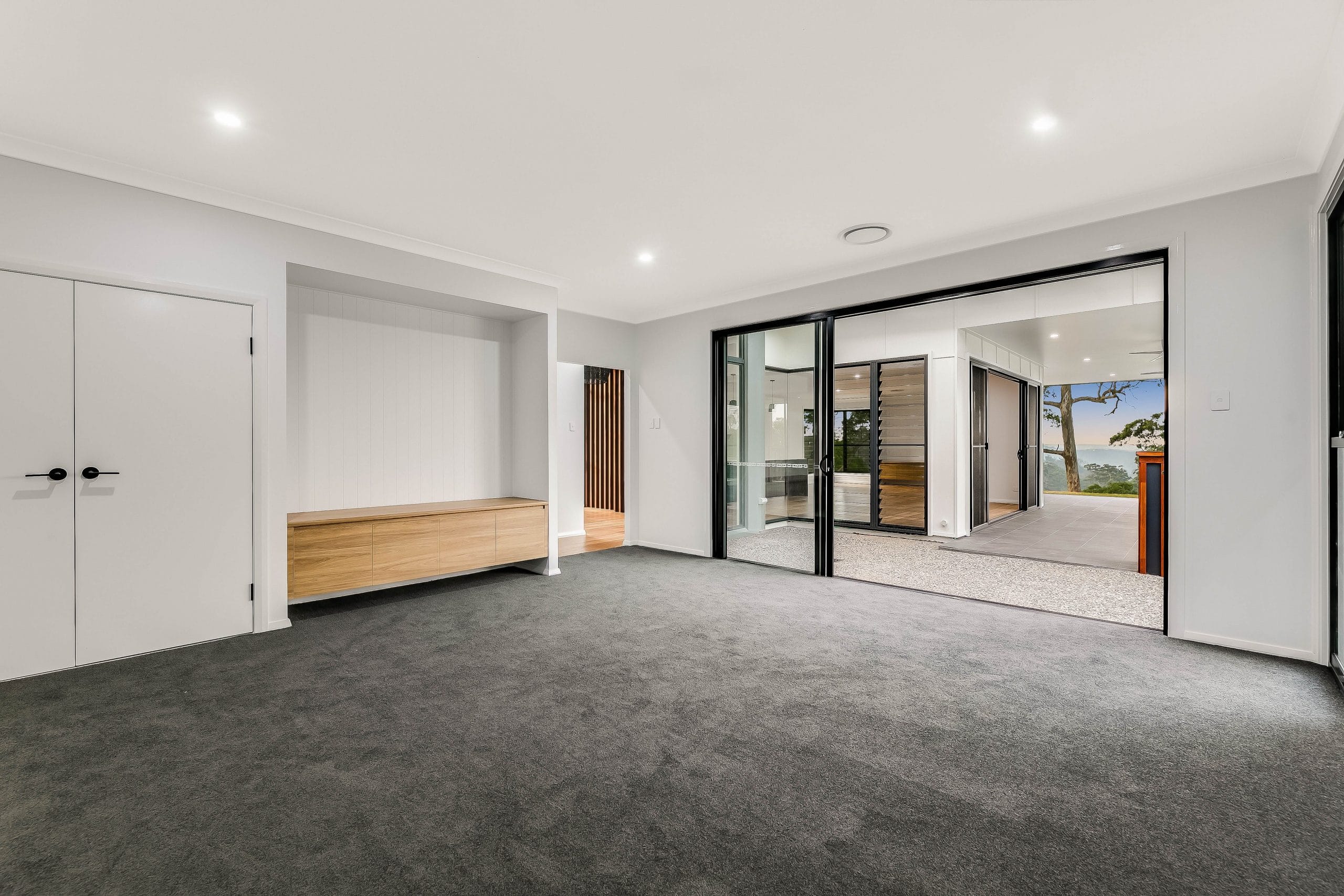 Empty bedroom with grey carpets, timber seat and sliding black doors