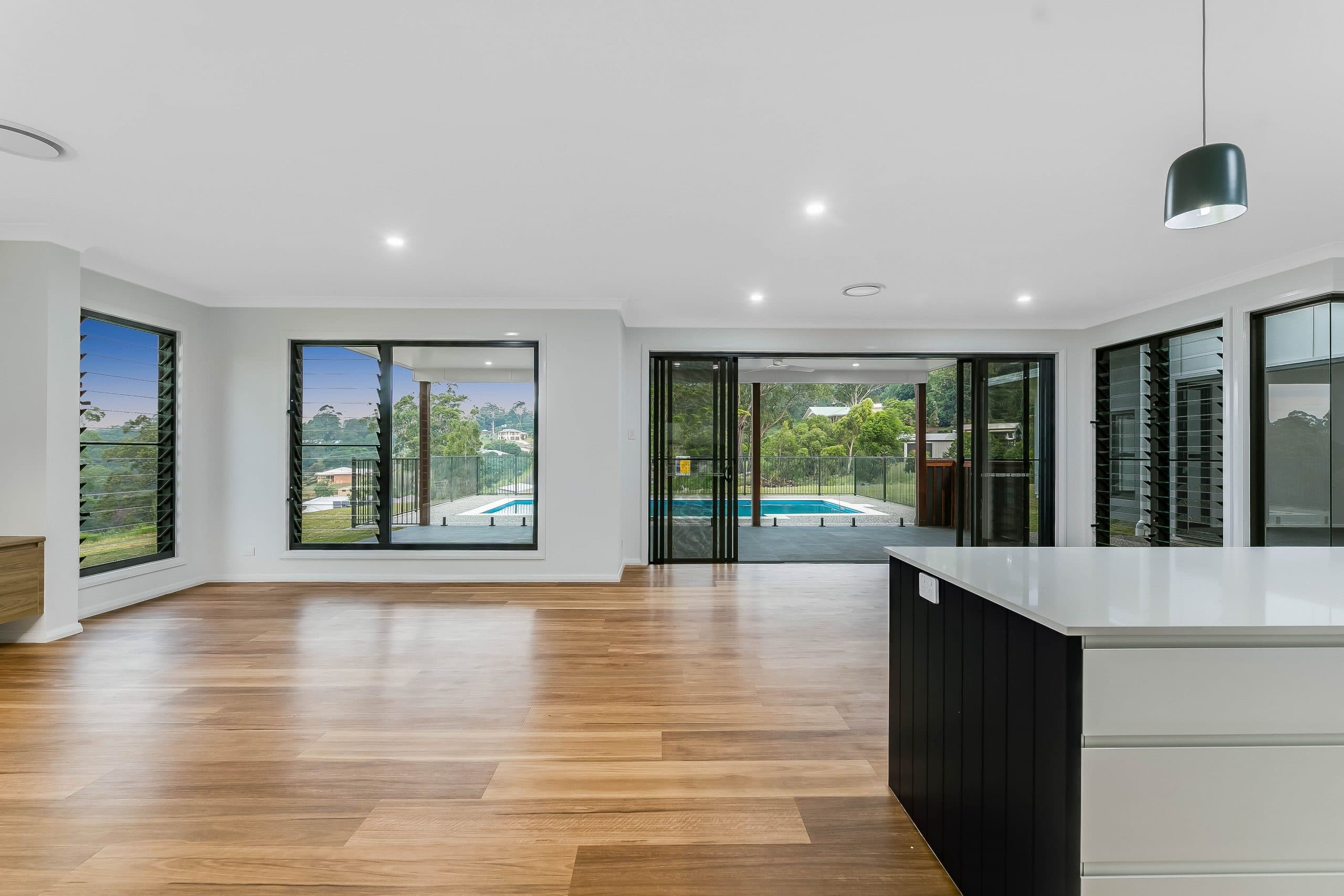 A wide open living area with open windows and sliding doors, looking out over a patio and pool