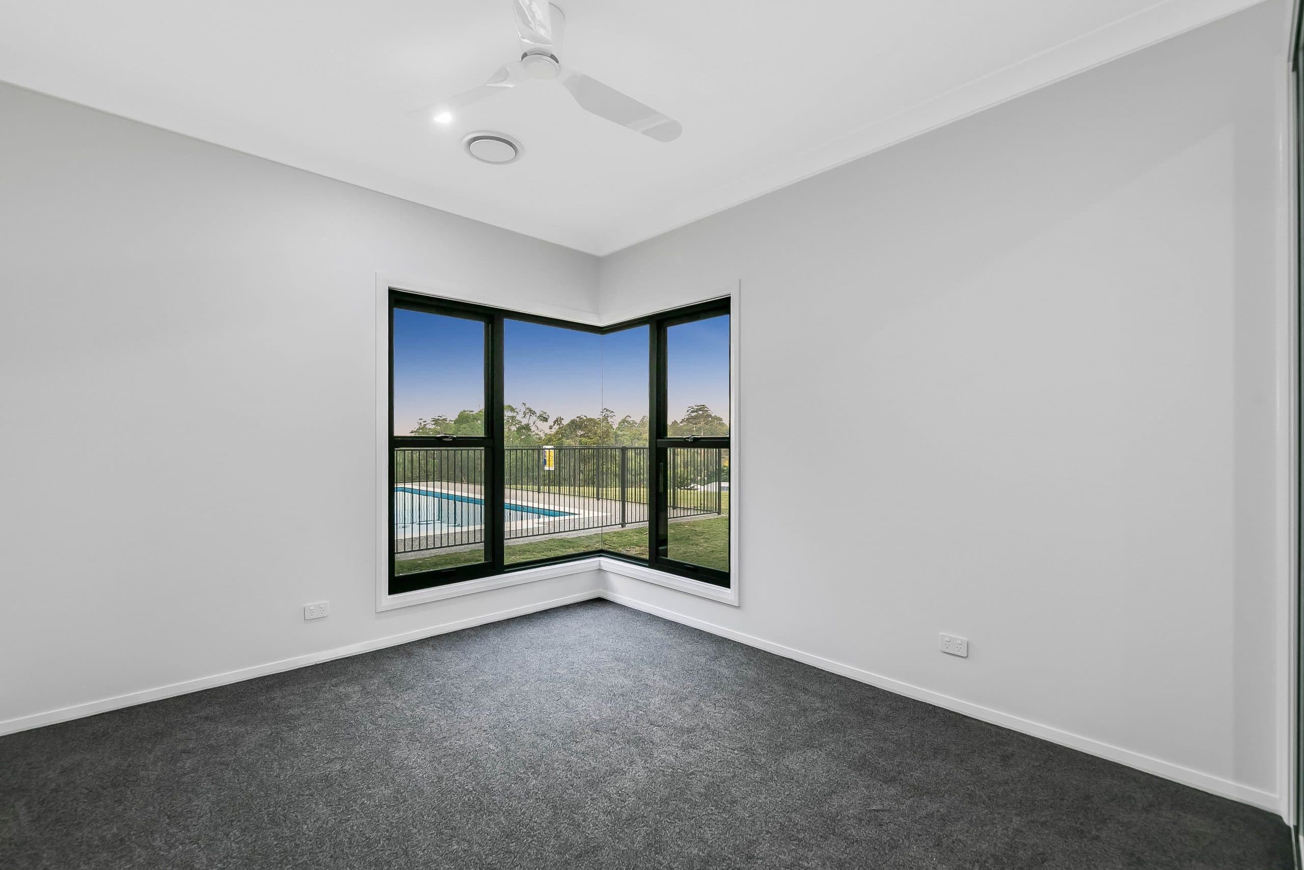 Empty room with white walls, grey carpet, black windowsills and overhead fan.